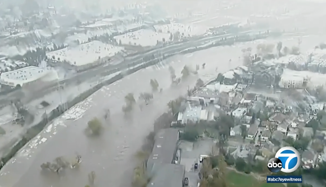 Full to almost overflowing concrete chute for the LA River, flows in an elbow past Atwater Village in Los Angeles in an aerial shot